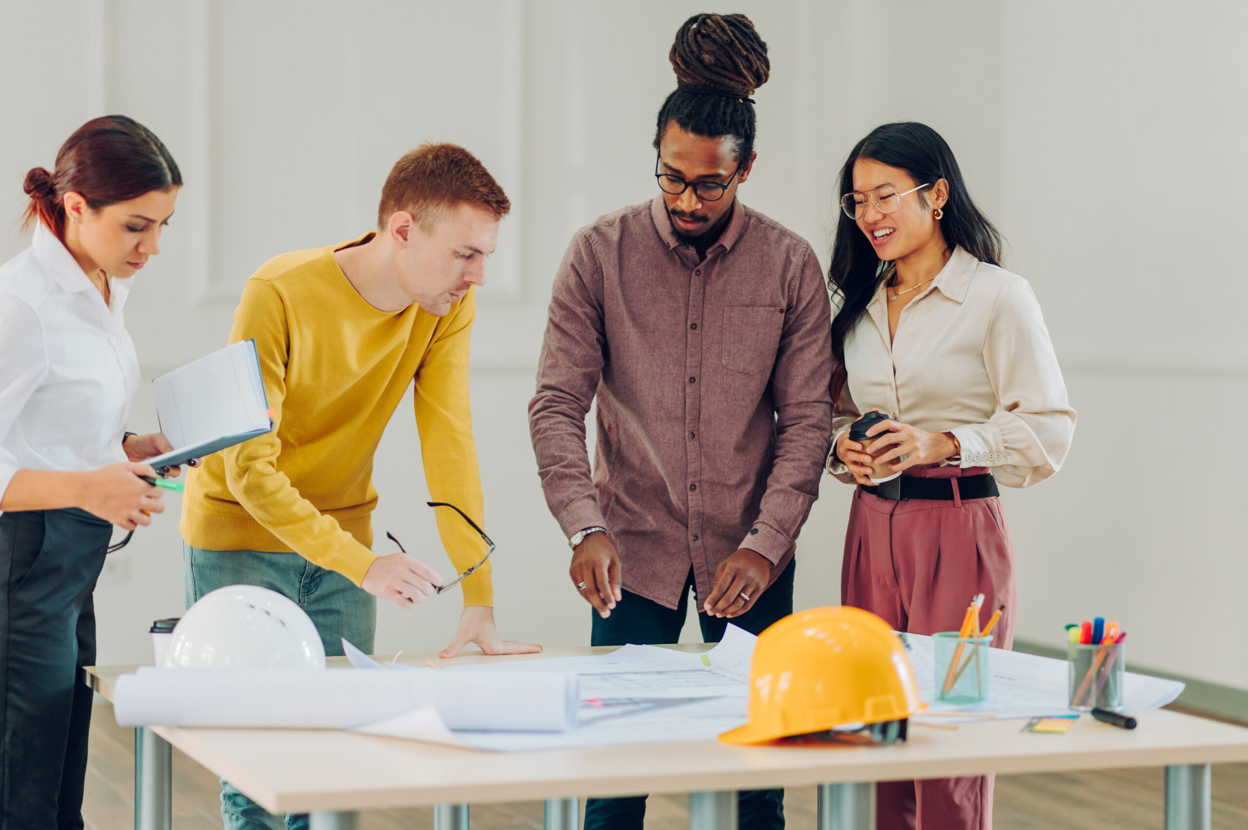 Diverse group of male and female engineers brainstorming together over a building project they are working on while sharing new construction ideas. Focus on an arabic team leader with dreadlocks.